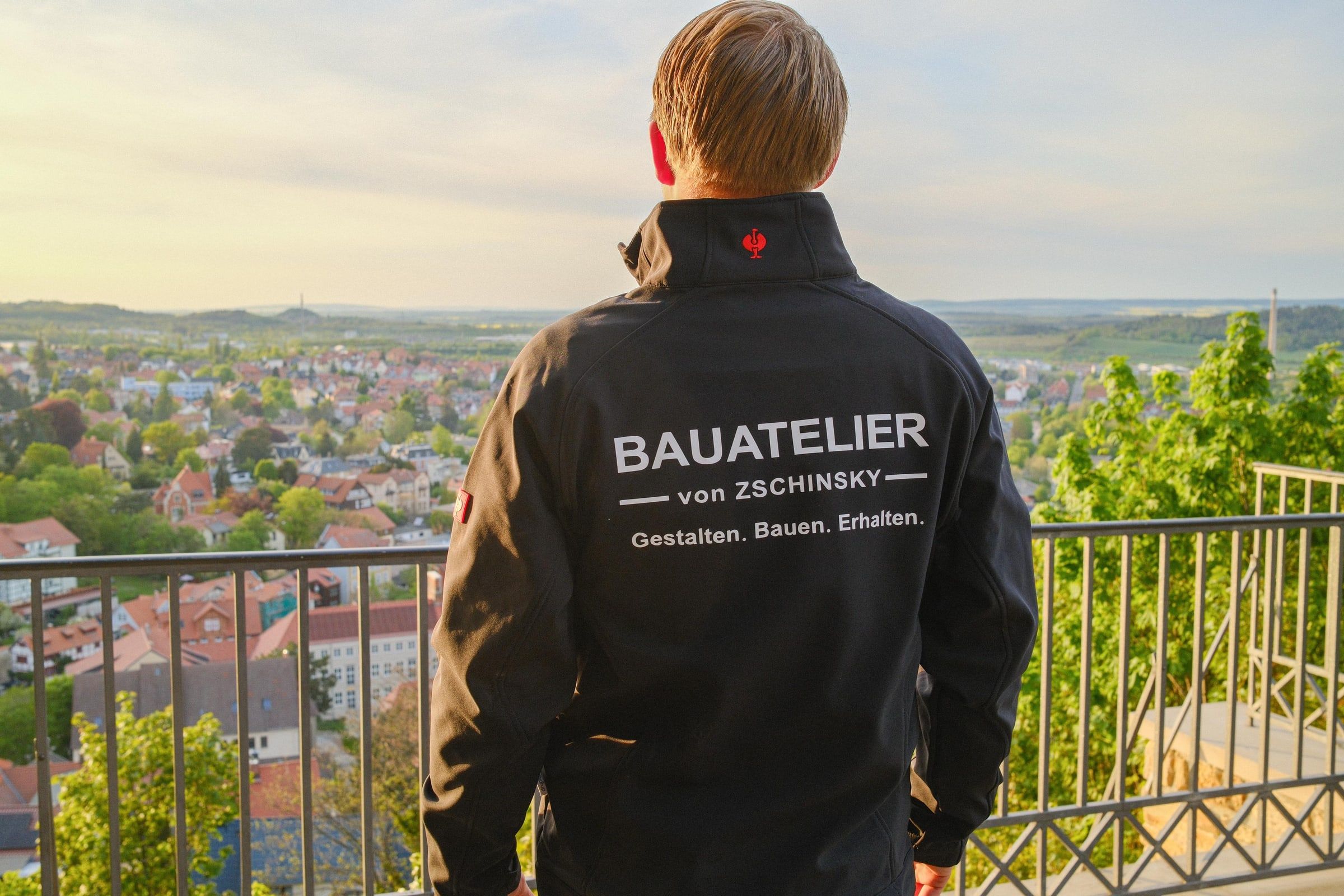 Herr von Zschinsky in der Firmenjacke des Bauateliers mit Blick über Blankenburg (Harz) am Abend