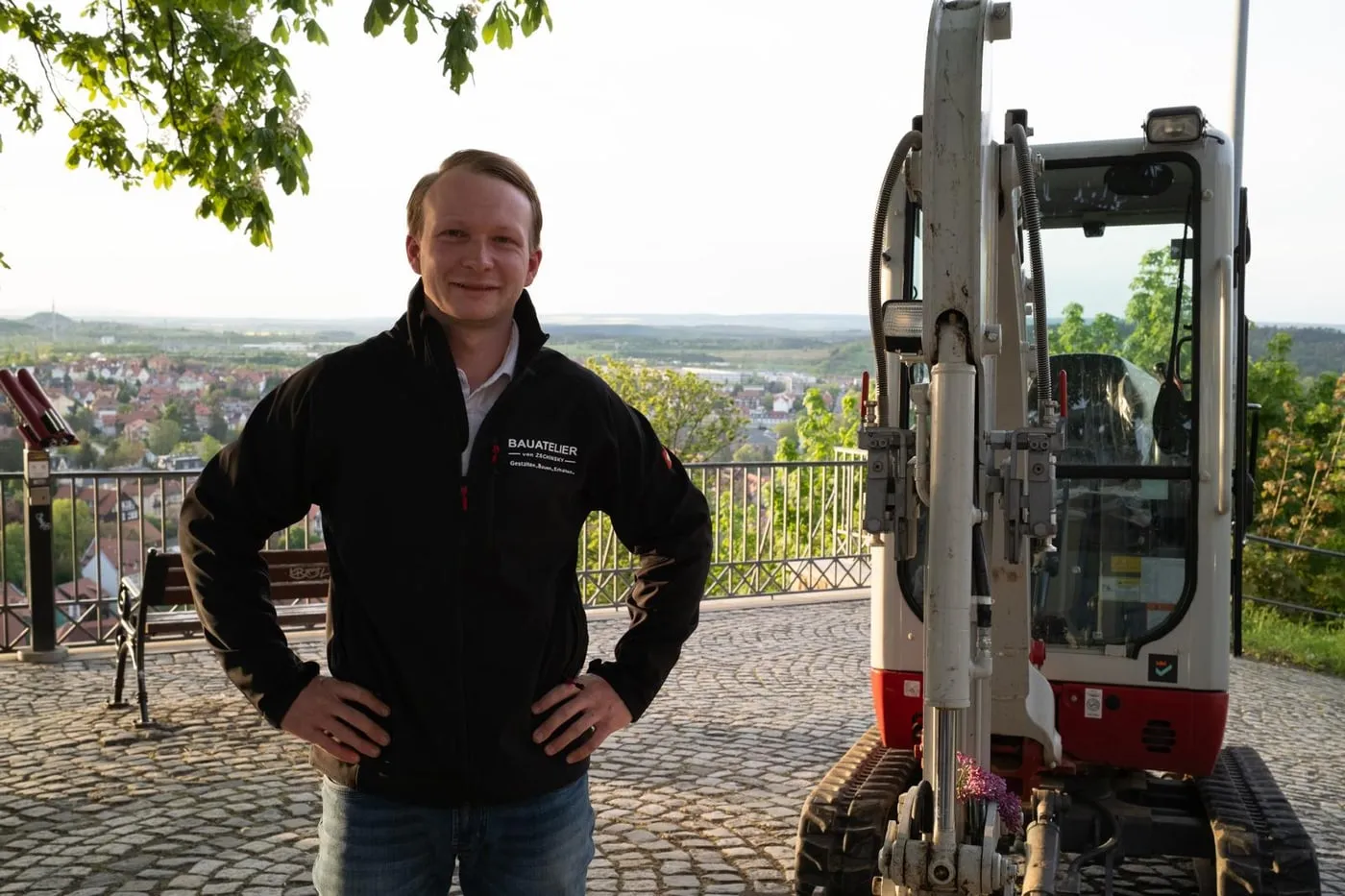 Rudi von Zschinsky, Maurermeister und Inhaber, auf einem Aussichtspunkt über dem Harz neben seinem Minibagger